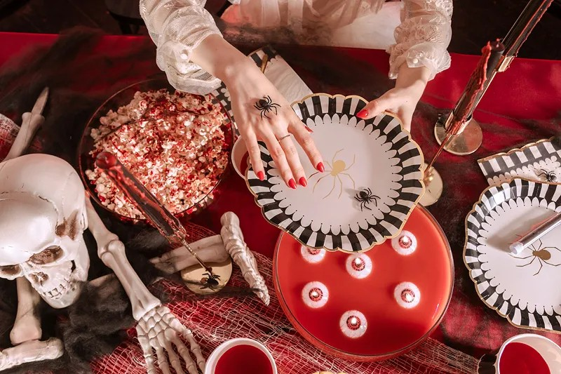 Halloween-themed table setting with decorative plates, skeleton hands, and spider webs.