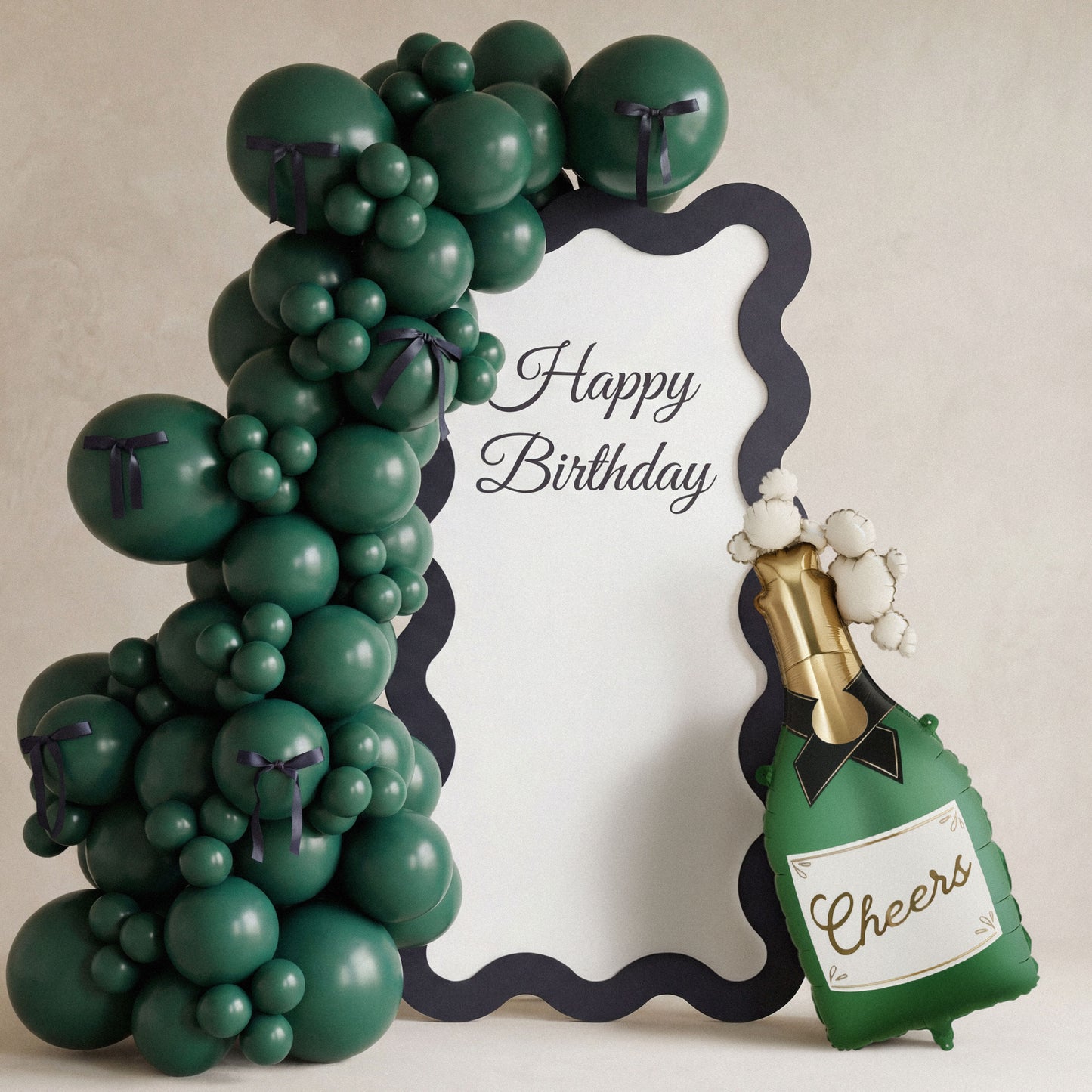 Green balloon arch with a 'Happy Birthday' sign and a bottle-shaped balloon with 'Cheers' text on a beige background.