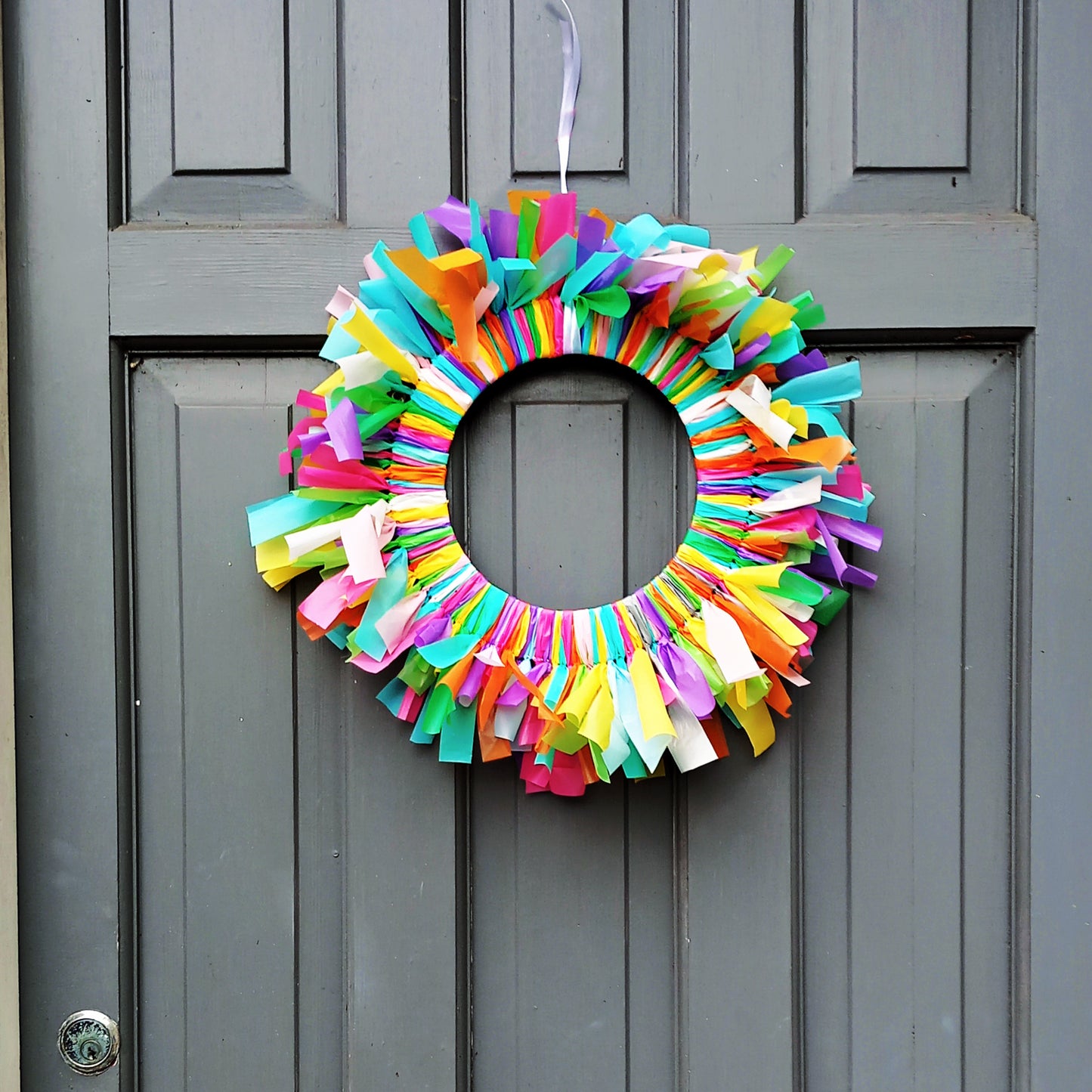 Colourful birthday door wreath hanging on a white front door, handmade party decoration.