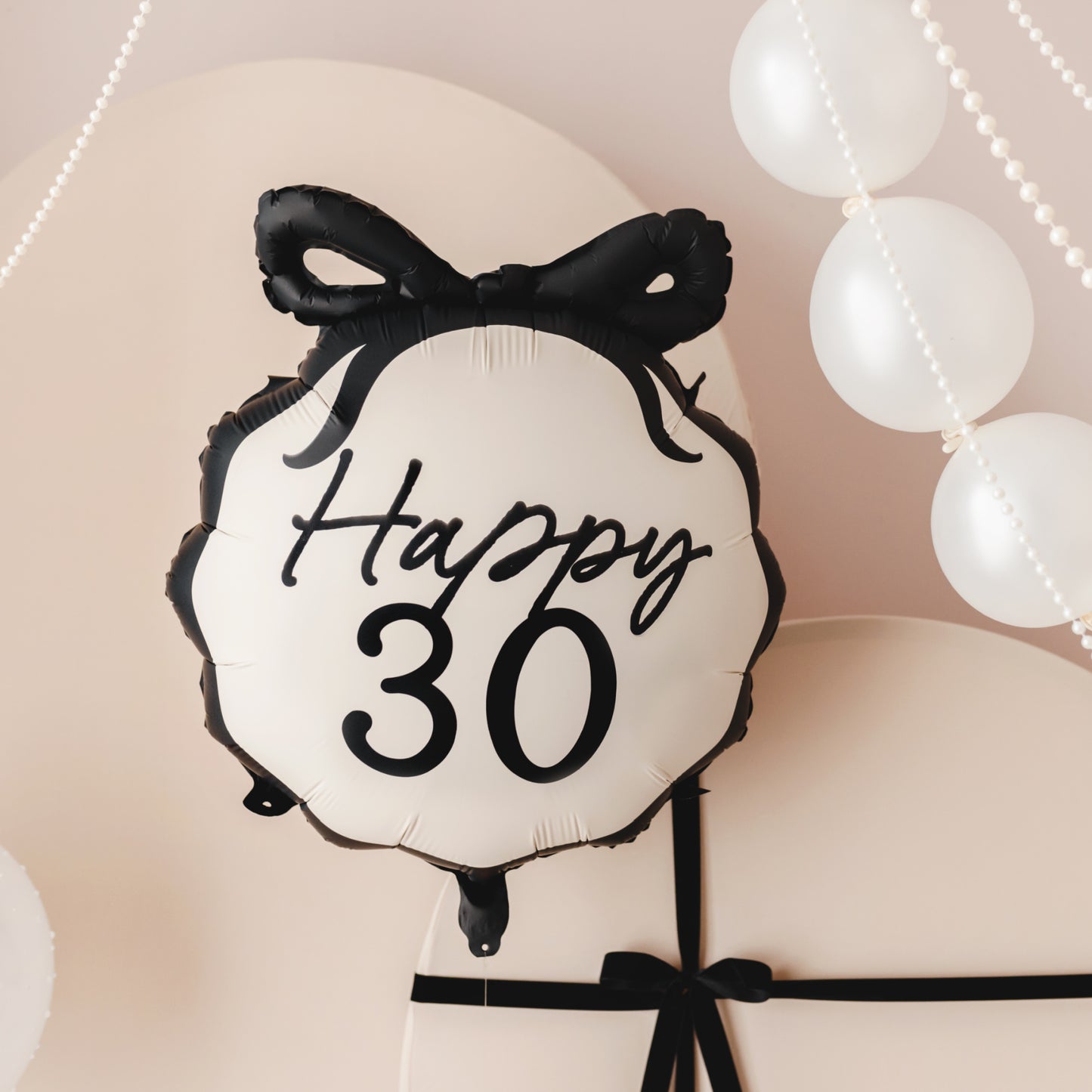 Balloon with 'Happy 30' text and black bow against a soft pink background