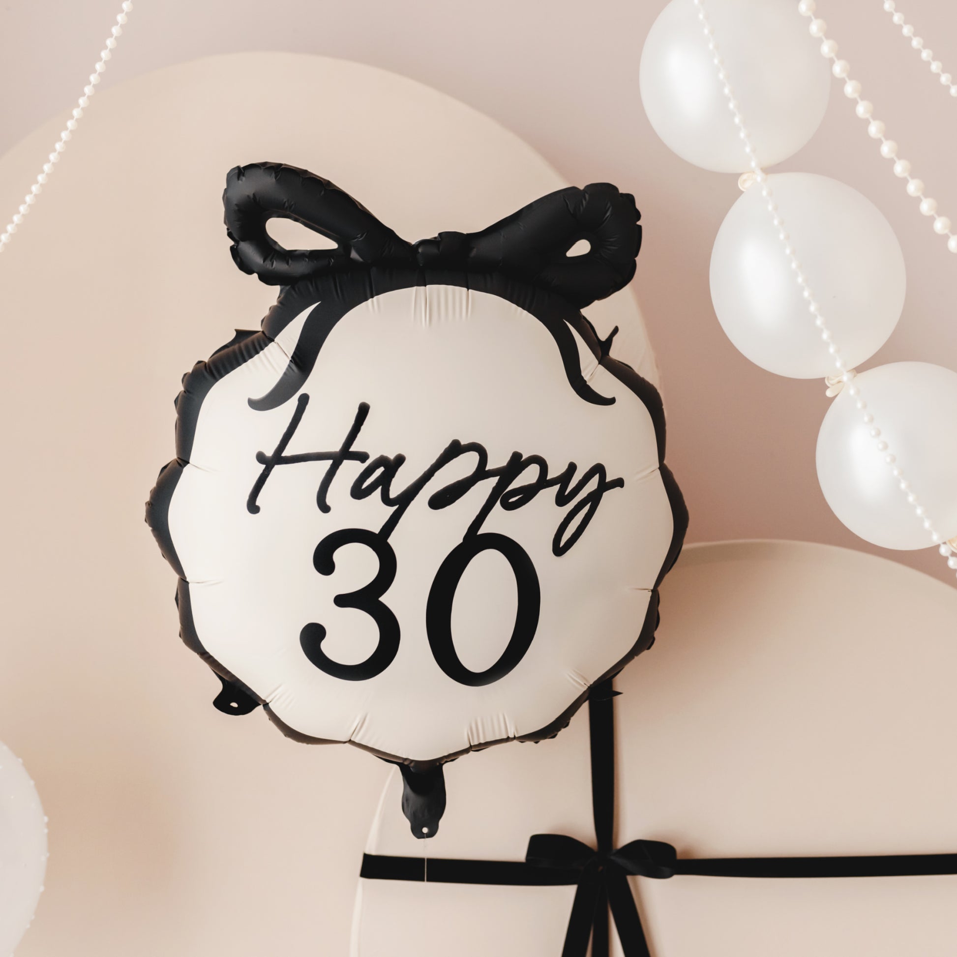 Balloon with 'Happy 30' text and black bow against a soft pink background