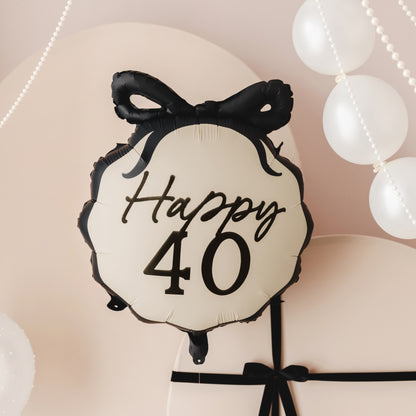 Round balloon with 'Happy 40' text and black bow against a soft pink background