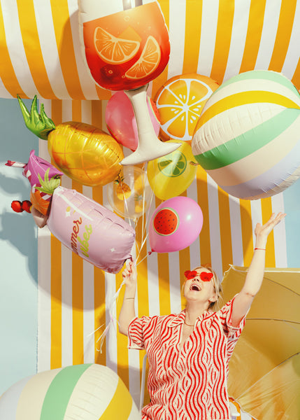 Woman with colorful fruit-themed balloons against a striped background