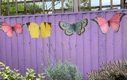 Butterfly-shaped decorations on a purple wooden fence with plants in the foreground.