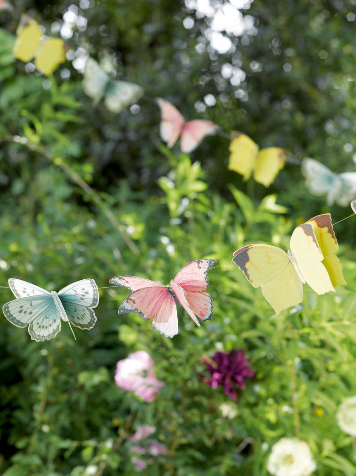Butterfly-shaped decorations on a string against a green garden background