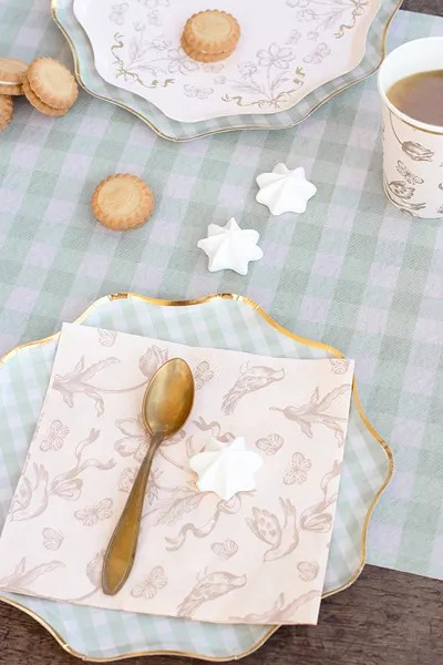 Table setting with a decorative plate, napkin, spoon, and cookies on a checkered tablecloth.