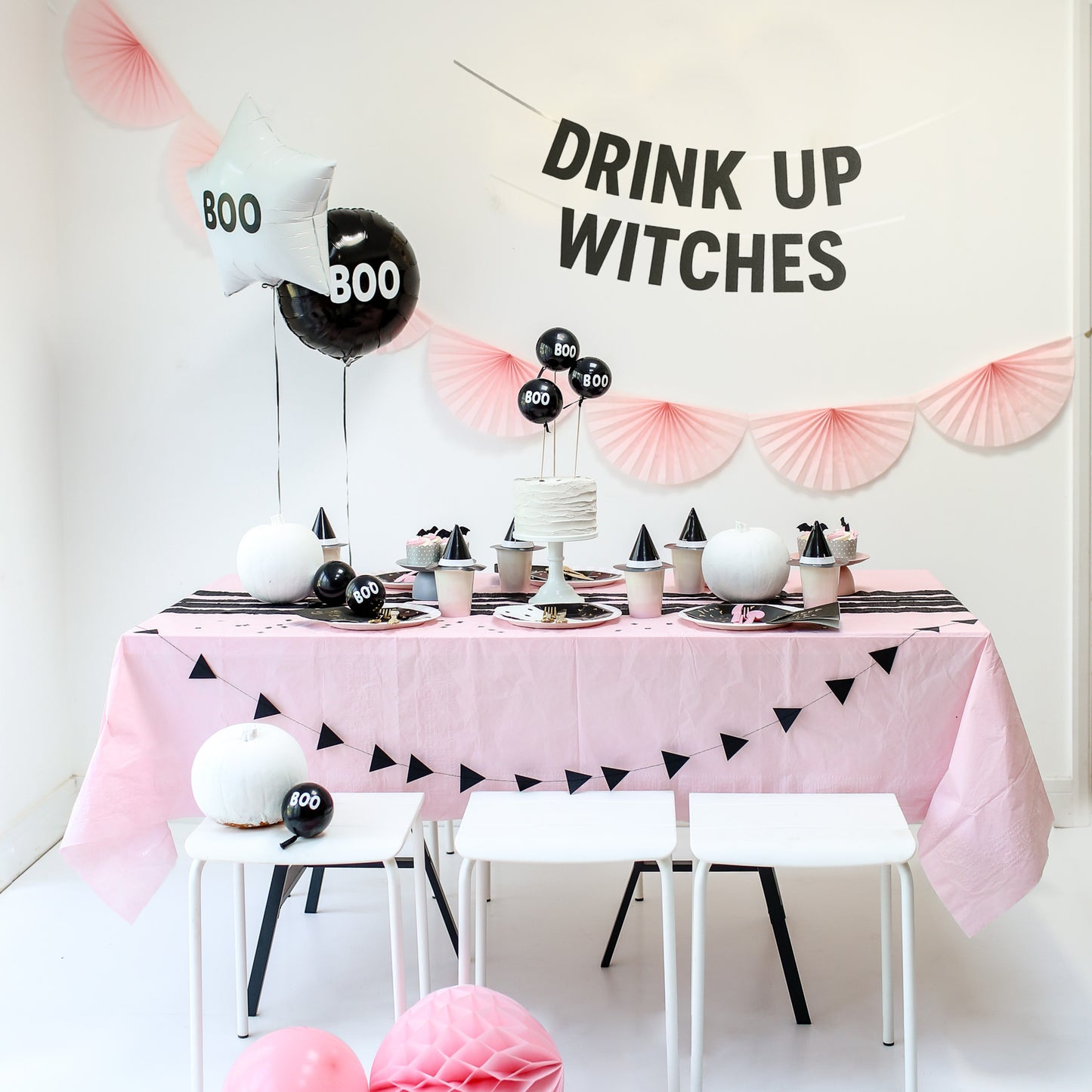 Halloween-themed table setting with pink tablecloth, black and white decor, and 'Drink Up Witches' sign.