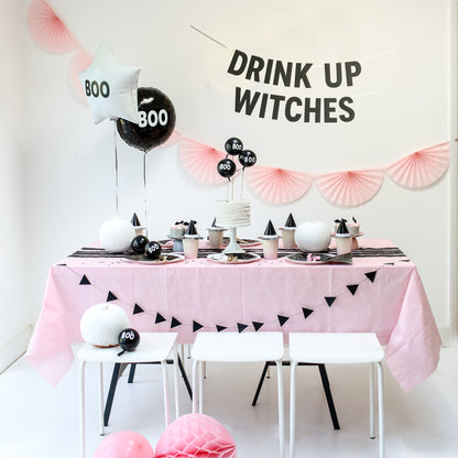Halloween-themed table setting with pink tablecloth, black and white decor, and 'Drink Up Witches' sign.