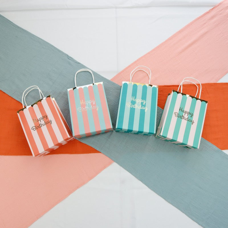 Four striped paper bags with 'Happy Birthday' text on a colorful geometric background