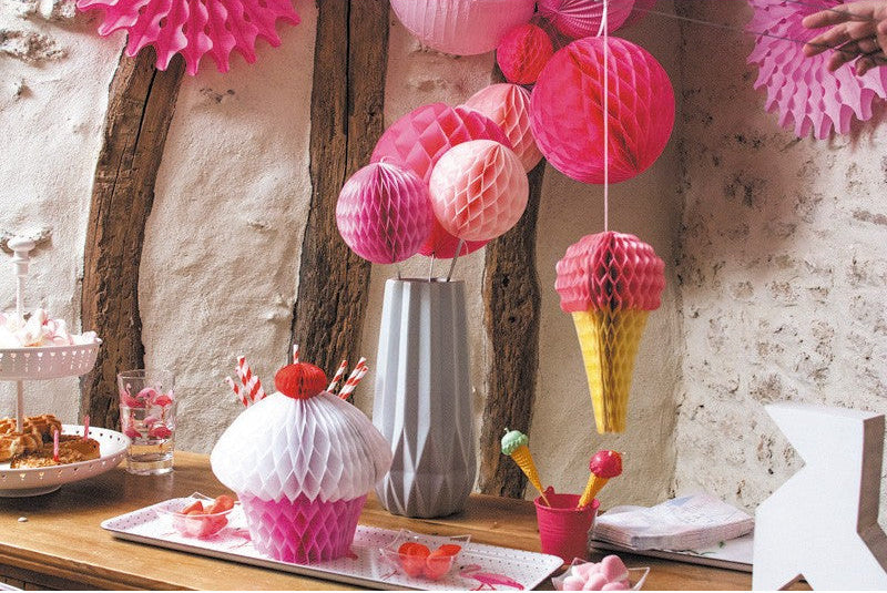 Decorative ice cream cone and cupcake-shaped items on a table with hanging pink paper lanterns.