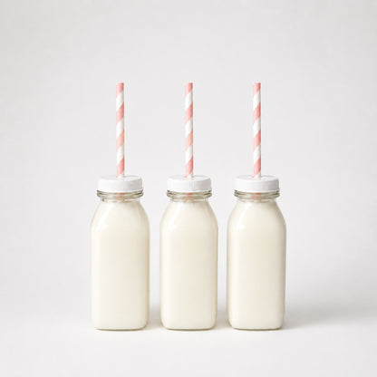 Mini plastic drinks bottles filled with milk with pink striped paper straws